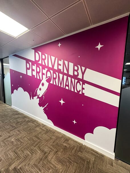 An image of the purple "Driven by Performance" wall graphic showing clouds, stars, and a spaceship.